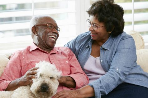 Happy Senior Couple Sitting On Sofa With Dog